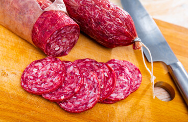 Slices of popular spanish dry-cured sausage with flavorful taste from minced Iberian pork seasoned with natural marinades without paprika on wooden board..