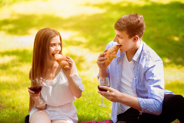 Naklejka premium Affectionate young couple eating croissants and drinking wine on picnic at park