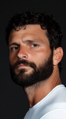 Obraz premium Close-up studio portrait of a handsome, dark-haired man with a full beard gazing intently.