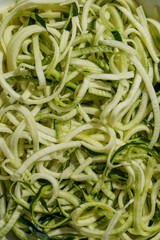Fresh zucchini noodles (zoodles) in a white enamel dish, ready for a healthy meal