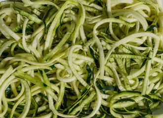 Fresh zucchini noodles (zoodles) in a white enamel dish, ready for a healthy meal