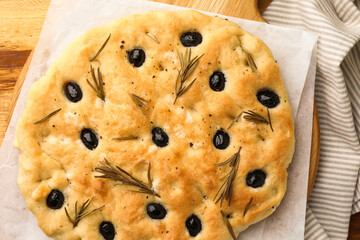 Delicious focaccia bread with olives and rosemary on wooden table, top view