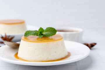 Tasty pudding with caramel sauce served on white tiled table, closeup