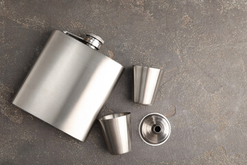 Hip flask, cups and funnel on grey table, flat lay. Space for text