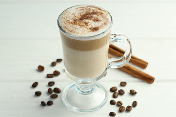 Tasty latte macchiato in glass cup, coffee beans and cinnamon on white wooden table, closeup