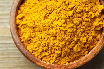 Turmeric powder in bowl on wooden table, top view