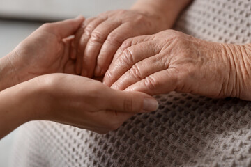 Fototapeta premium Caregiver supporting senior woman on light background, closeup. Elderly care