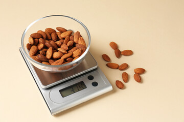 Electronic kitchen scale with almonds on beige background
