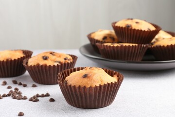 Delicious muffin with chocolate chips on light grey table, closeup