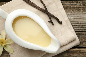 Tasty condensed milk, vanilla pods and flower on wooden table, flat lay
