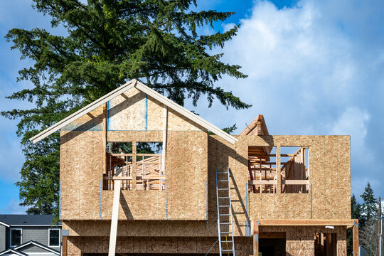 New home construction site, aluminum extension ladder to second story, framing and oriented strand board (OSB) exterior wall, housing development on a sunny winter day
