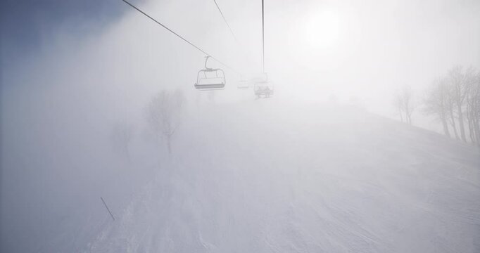 POV on snowy mountain ski lift with thick fog