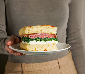 woman hand holding a focaccia bread italian sandwich, Porchetta meat, kale, mozzarella, pesto, sun...