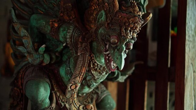 Balinese traditional carved wooden statue stands in traditional wooden house illuminated by light