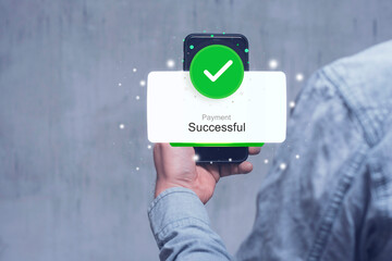 A Man in a denim sleeve holds a smartphone displaying a Payment Successful notification with a green checkmark against a blurred background. © vadish