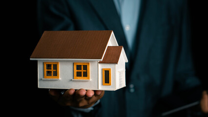 Businessman holding model house showing real estate market growth, real estate and investment concept, real estate market analysis or economic development concept.