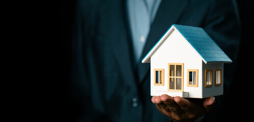 Businessman holding model house showing real estate market growth, real estate and investment concept, real estate market analysis or economic development concept.