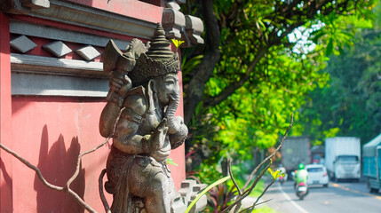 An old hindu stone statue of Ganesha covered with moss, standing on the street on the Bali