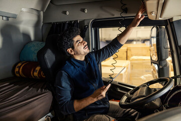 Interracial truck driver sitting in truck with tablet in hands and doing inspection.