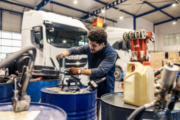 Young interracial workman attaching pump on oil barrel at auto mechanic workshop.
