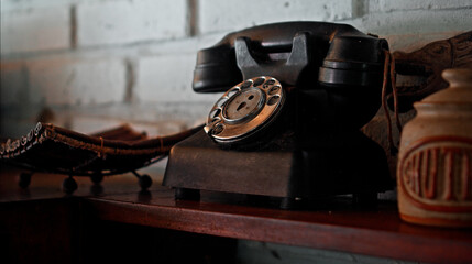 An antique telephone with a mechanical rotating keypad sits on a wooden table