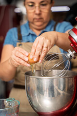 Pastry chef cracking eggs into stand mixer for dessert preparation
