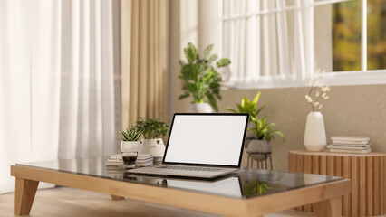 The white screen laptop on wooden table with decors placing under the window in the bright room.