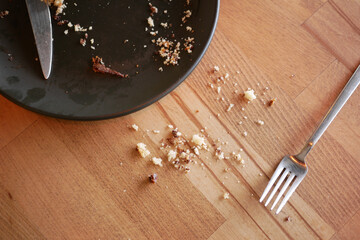 Crumbs and utensils left on a wooden table after a meal