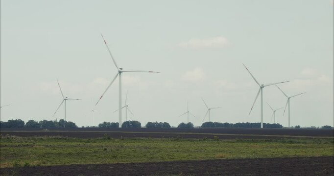 Wind turbines rotating in agricultural landscape under cloudy sky