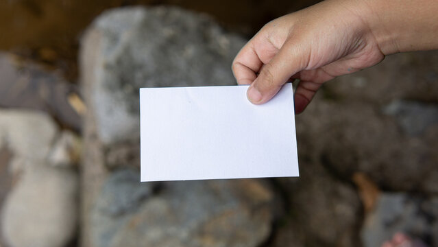 A pristine white card with a smooth texture is held by tiny hands, set against the backdrop of a large, sturdy stone