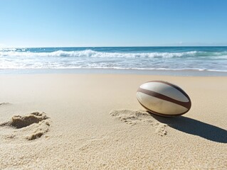 A rugby ball resting on golden beach sand, with the ocean waves and clear blue sky creating a serene coastal atmosphere.