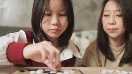 Fototapeta premium Close-up shot, Asian family times, mom, and kid fun playing Go, checkers board game on table in home living room together with love and cheerful, happy weekend relaxing hobby of child and parent.
