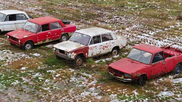 Old, Russian deteriorating vehicles from the Soviet era rest in an open, drone
