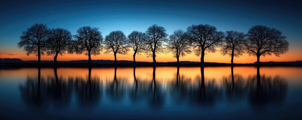 Fototapeta premium Lakeside sunset landscapes idea. Stunning landscape at sunset with silhouetted trees and calm water reflection.