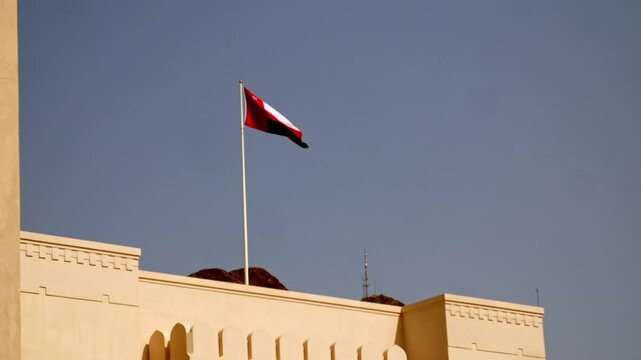 Oman flag waiving at wind standing above the islamic building in the capital city of muscat