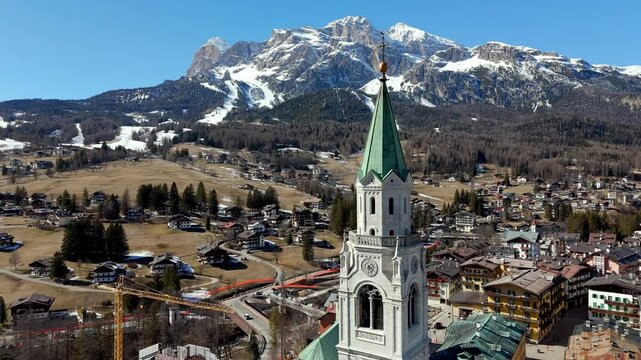 drone fly close to cortina d ampezzo church old bell tower with village and dolomite mountains landscape in background