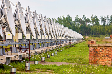 A row of solar radio telescope dishes against a forest background