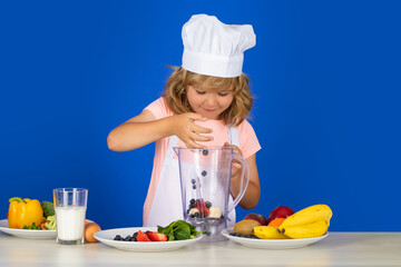 Portrait of a 7, 8 years old child in cook cap and apron making fruit salad and cooking food in kitchen. Cute little blonde happy smiling chef.