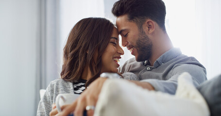 Fototapeta premium Comfortable, laughing and couple with coffee, home and love in living room with woman, hug and bonding. Happy, man and forehead touch with partner in lounge, tea and chilling in house or relationship