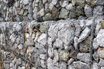 gabion wall, showcasing the texture of the grey stones and the wire mesh. The image highlights the detailed pattern and rugged nature