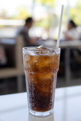 A glass of ice-cold cola sits on a table, condensation glistening on the glass.