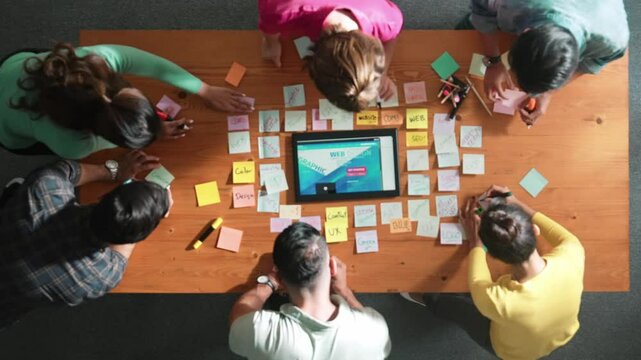 Top down view of programmer brainstorming and planning about web design while looking at tablet wireframe prototype. Aerial view of skilled developer team talking about digital application. Symposium.