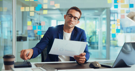 Businessman, documents and analysis with laptop for finance or company performance at office desk. Man, employee or analytics with paperwork for graph, chart or data on business growth at workplace