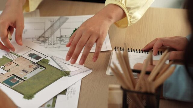 Architects using measurement tool and pencil tracing in building blueprint by coworker support on table with architectural document and wooden block scatter around at office. Closeup. Delineation.