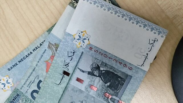 Several Malaysian banknotes of various denominations are placed one by one on a beige-colored table, showcasing the currency's distinct features and intricate designs.