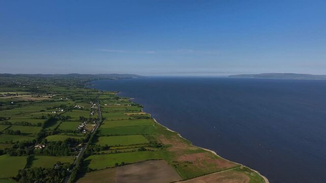 Lough Foyle, County Donegal, Ireland, June 2023. Drone pushes forwards in panoramic aerial view following the lake shore under an open blue sky with a scenic backdrop of the beautiful lake.