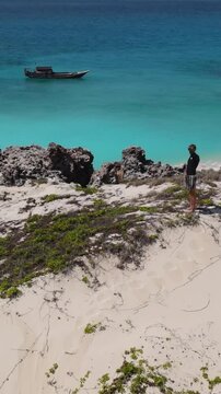 Male traveler exploring a desert island.Standing on a hill and looking into the distance of the Indian Ocean.Yaght at background