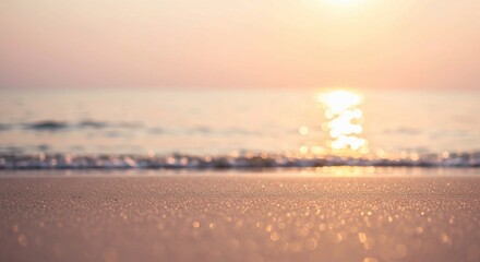 Obraz premium The image features a close-up of sandy beach texture with a blurred ocean background captured in warm golden light, creating a tranquil scene