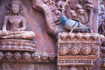 Fototapeta premium Ornate stone carvings with a pigeon perched, featuring a serene seated figure and intricate details