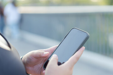 Portrait of A person holds a smartphone outdoors, focused on the screen while standing near a railing in a blurred background. plus size woman